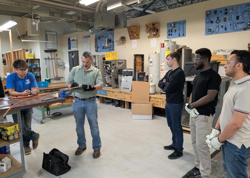 A group of students watch a demonstration with a copper pipe