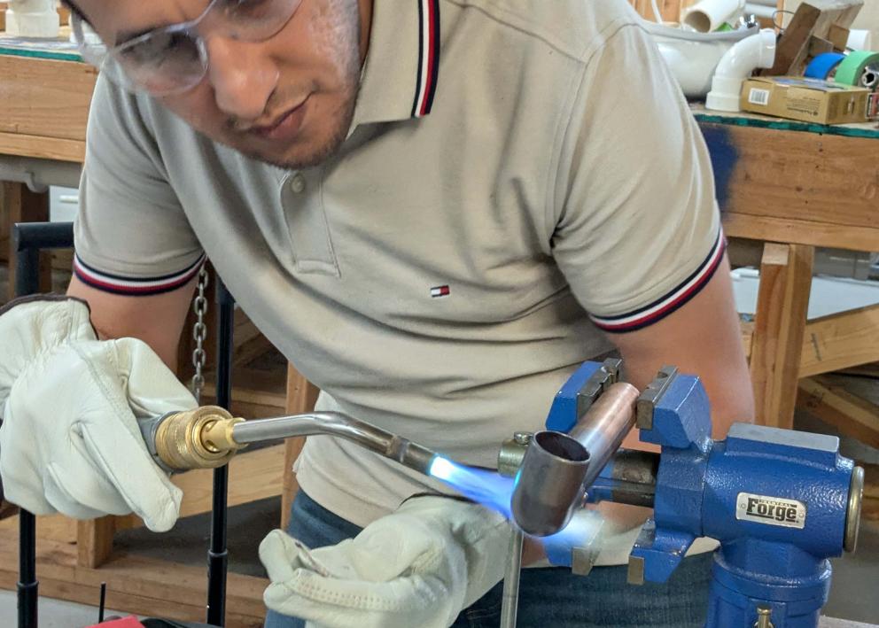 A student with goggles welding on a copper pipe in a vise