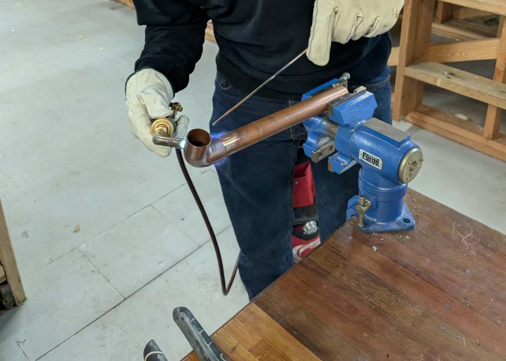 A student wearing goggles welding on a copper pipe