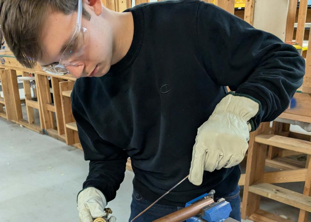 A student wearing goggles welding on a copper pipe