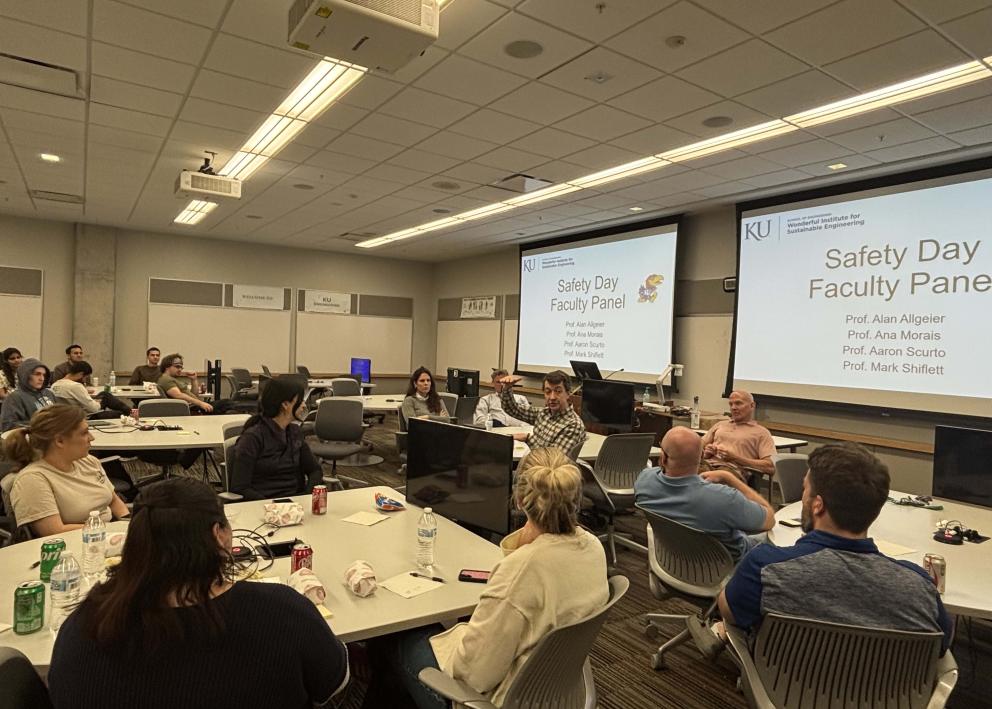 People sitting around tables in a room with screens the say "Safety Day Faculty Panel"