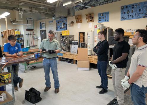 A group of students watch a demonstration with a copper pipe