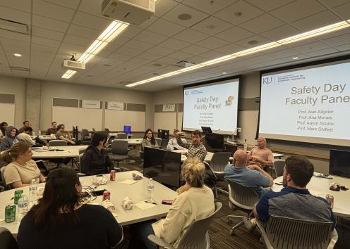 People sitting around tables in a room with screens the say "Safety Day Faculty Panel"