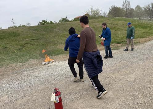 two people preparing to extinguish a small fire by the side of a gravel road